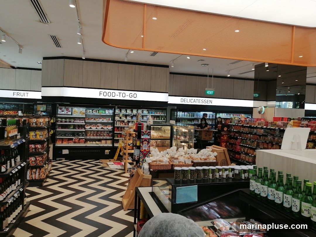 A view inside a supermarket with aisles stocked with various food items. Signs indicate sections for