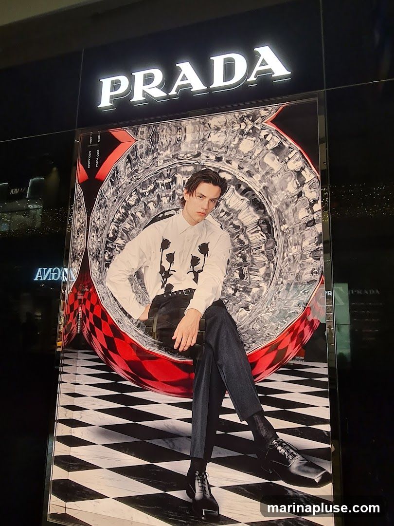 A large advertisement featuring a man sitting in a chair with a checkered pattern. The Prada logo is visible above the advertisement.