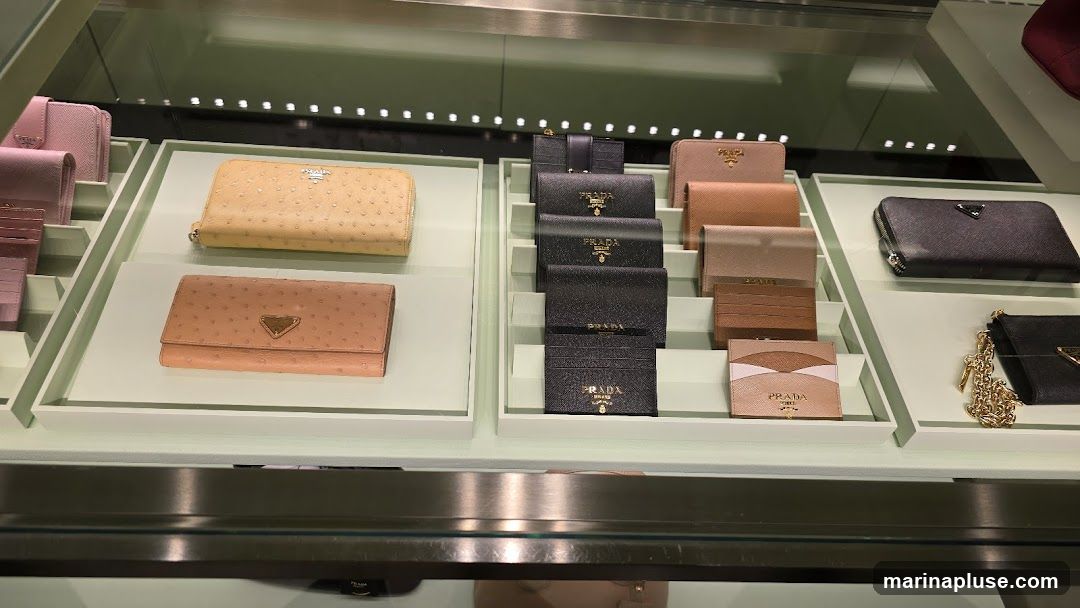 A display case filled with various Prada wallets and cardholders in different colors and textures, including ostrich leather.