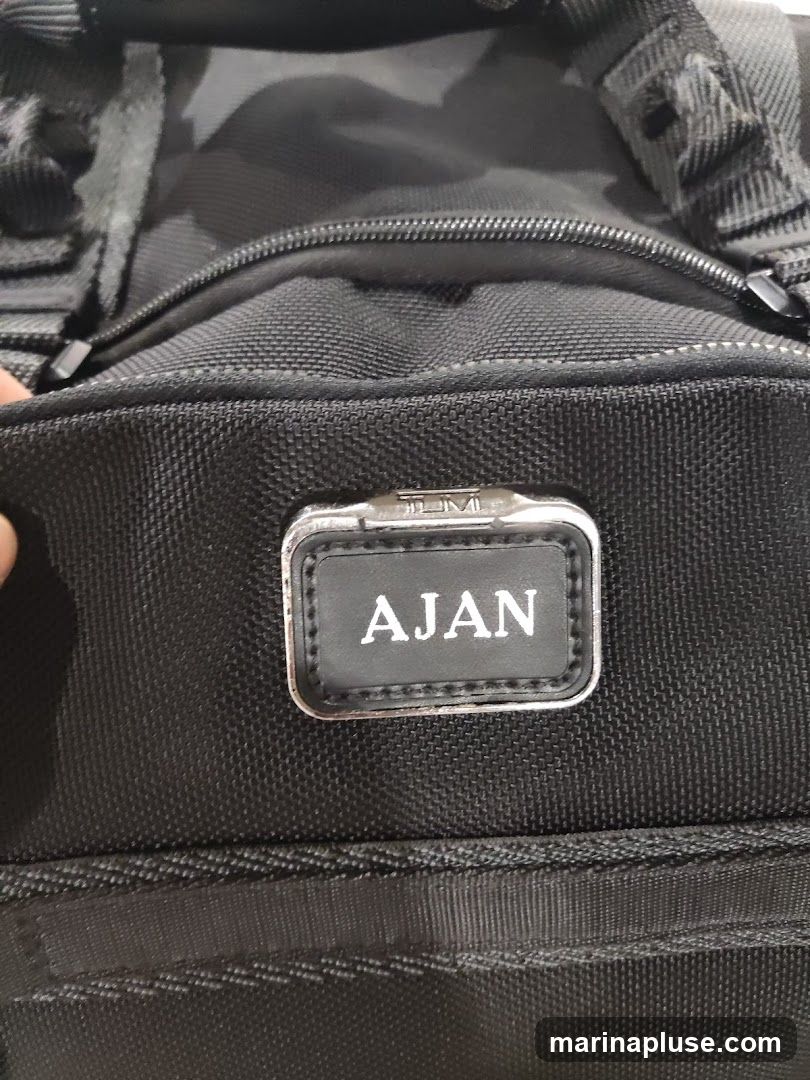 A close-up shot of a black fabric bag with a personalized tag that reads "AJAN" above the TUMI logo.