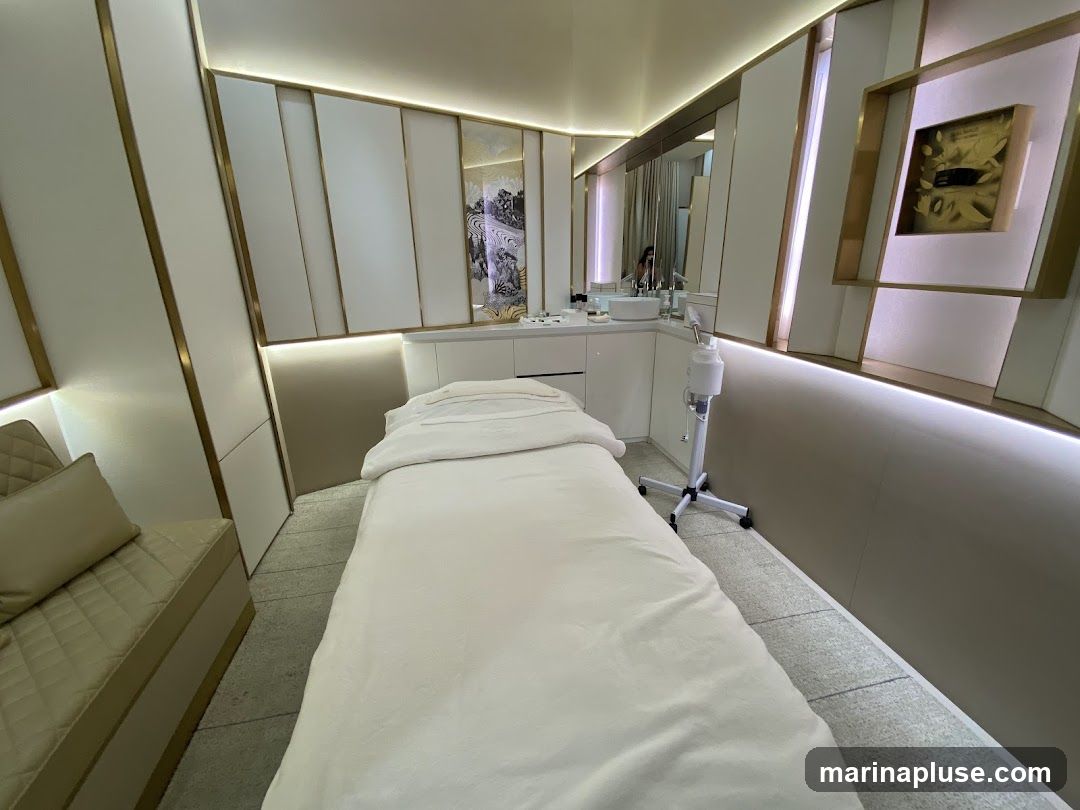 A clean and modern spa treatment room with a massage bed, a sink area, and decorative wall panels. The room is illuminated by soft, ambient lighting.