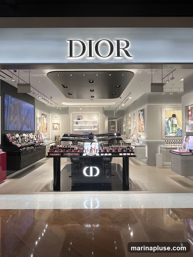 The exterior of a Dior cosmetics store. The large, illuminated DIOR logo is prominently displayed above the entrance. Inside, the store is well-lit and showcases a wide array of makeup and perfume products on display tables and shelves. The interior features a modern and luxurious design with clean lines and elegant displays.