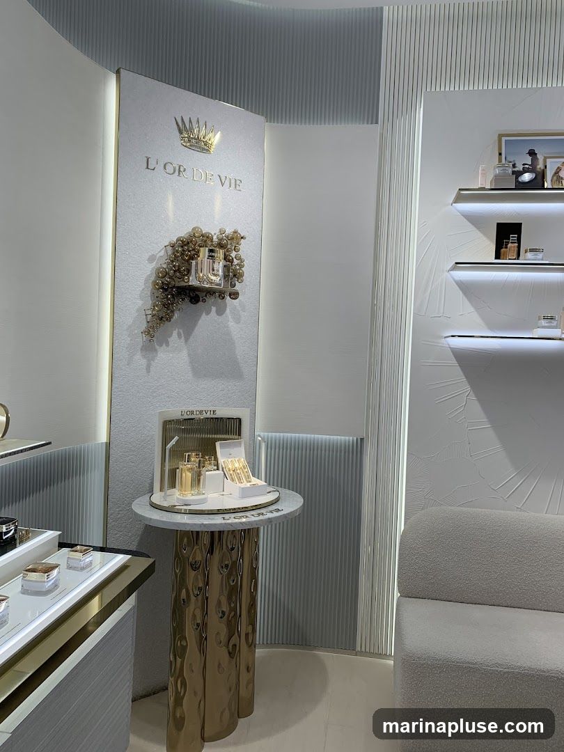 A luxurious display of cosmetics with the brand name L'OR DE VIE prominently featured. The display includes various perfume bottles and skincare products arranged on shelves and a decorative table. A plush white sofa is visible on the right side of the image.