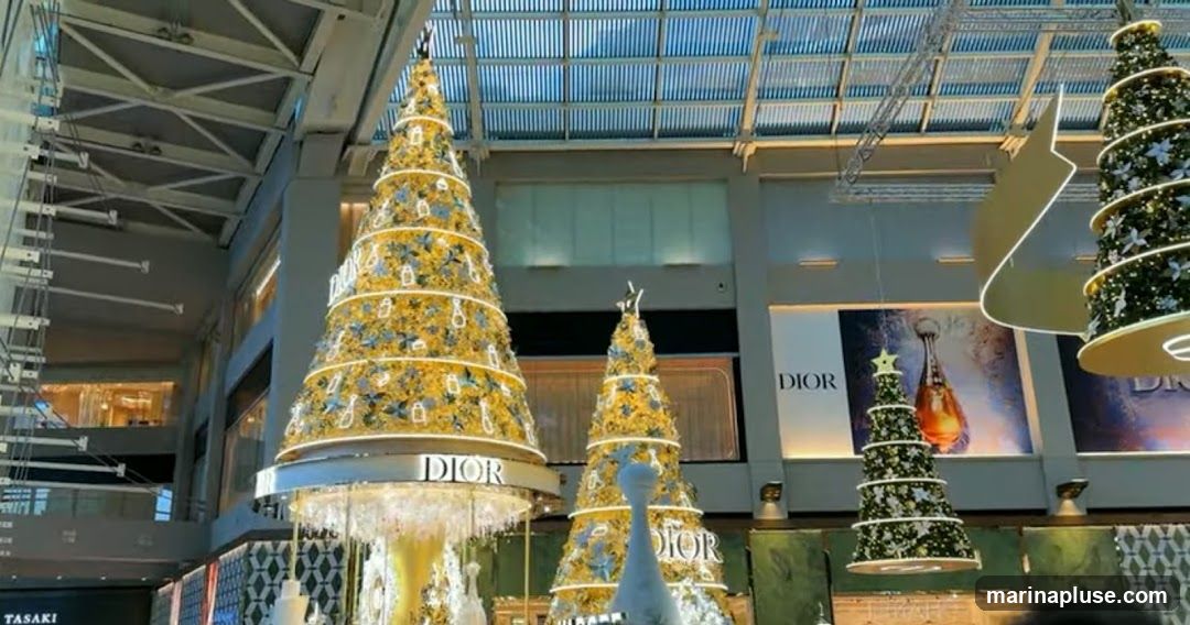 Large, elaborately decorated Christmas trees are displayed indoors, likely in a shopping mall. The trees are adorned with lights and ornaments, and the Dior logo is prominently featured on signage and on the trees themselves. One tree has a large Dior sign encircling its base. In the background, there are large advertisements for Dior products, including perfume bottles.