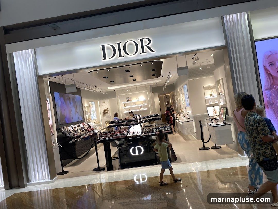The exterior of a Dior store with the brand name prominently displayed above the entrance. Inside, various makeup and beauty products are displayed on shelves and counters. Several customers are browsing the merchandise.