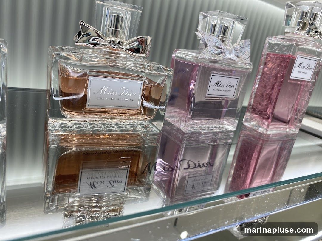 Several bottles of Miss Dior perfume are displayed on a reflective surface. The bottles are made of clear glass and contain pink and amber colored perfumes. Each bottle has a label with the Miss Dior logo and the name of the fragrance. Some bottles are adorned with bows.
