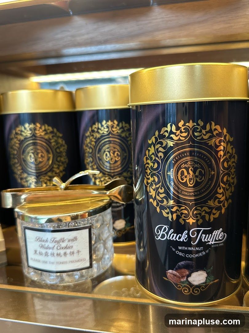 A close-up shot of tins and a jar of Black Truffle with Walnut Cookies. The main tin in focus is black with gold ornate designs and text that reads "Black Truffle with Walnut OSC COOKIES ESTD 1985". To the left, a glass jar with gold tongs contains cookies and has a label that reads "Black Truffle with Walnut Cookies" in English and Chinese.