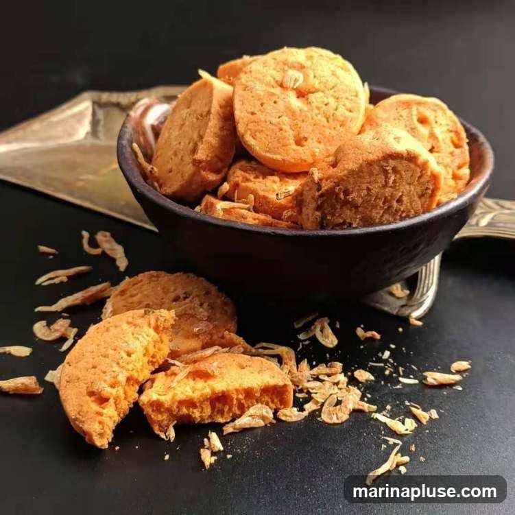 A bowl of shrimp crackers is shown, with some crackers spilled out onto a dark surface. Dried shrimp pieces are scattered around the crackers.
