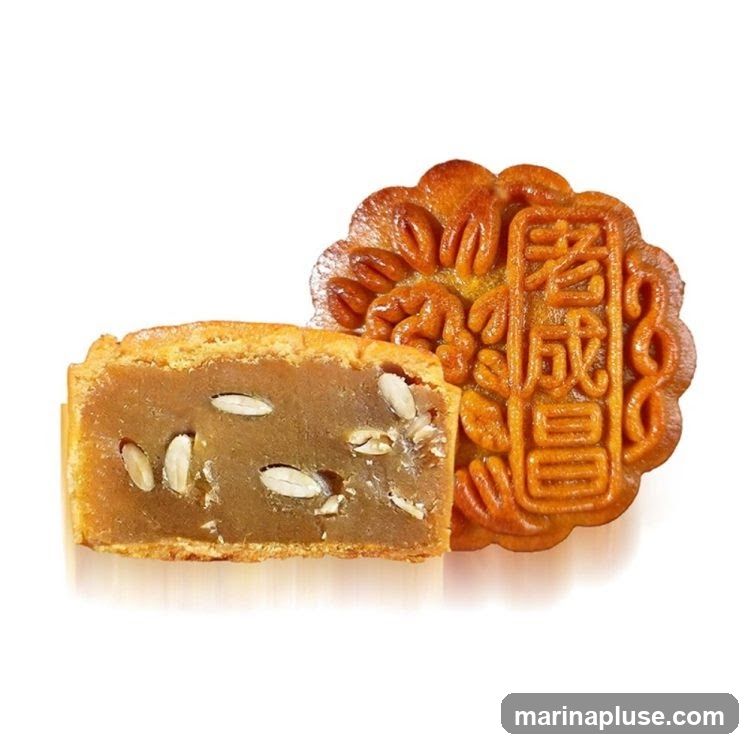 A close-up studio shot of a mooncake, with one half cut to reveal the filling. The mooncake has a golden-brown crust with intricate floral patterns and Chinese characters embossed on the top. The filling appears to be a light brown paste with visible white seeds or nuts.