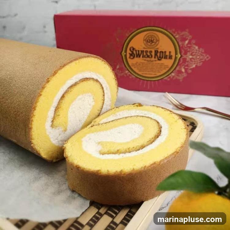 A close-up shot of a Swiss roll cake, with one whole roll and several slices on a serving platter. The cake has a light yellow sponge and a white cream filling. In the background, a red box with a circular logo that reads "Swiss Roll" is visible. A fork and a sprig of leaves with a citrus fruit are also in the frame.