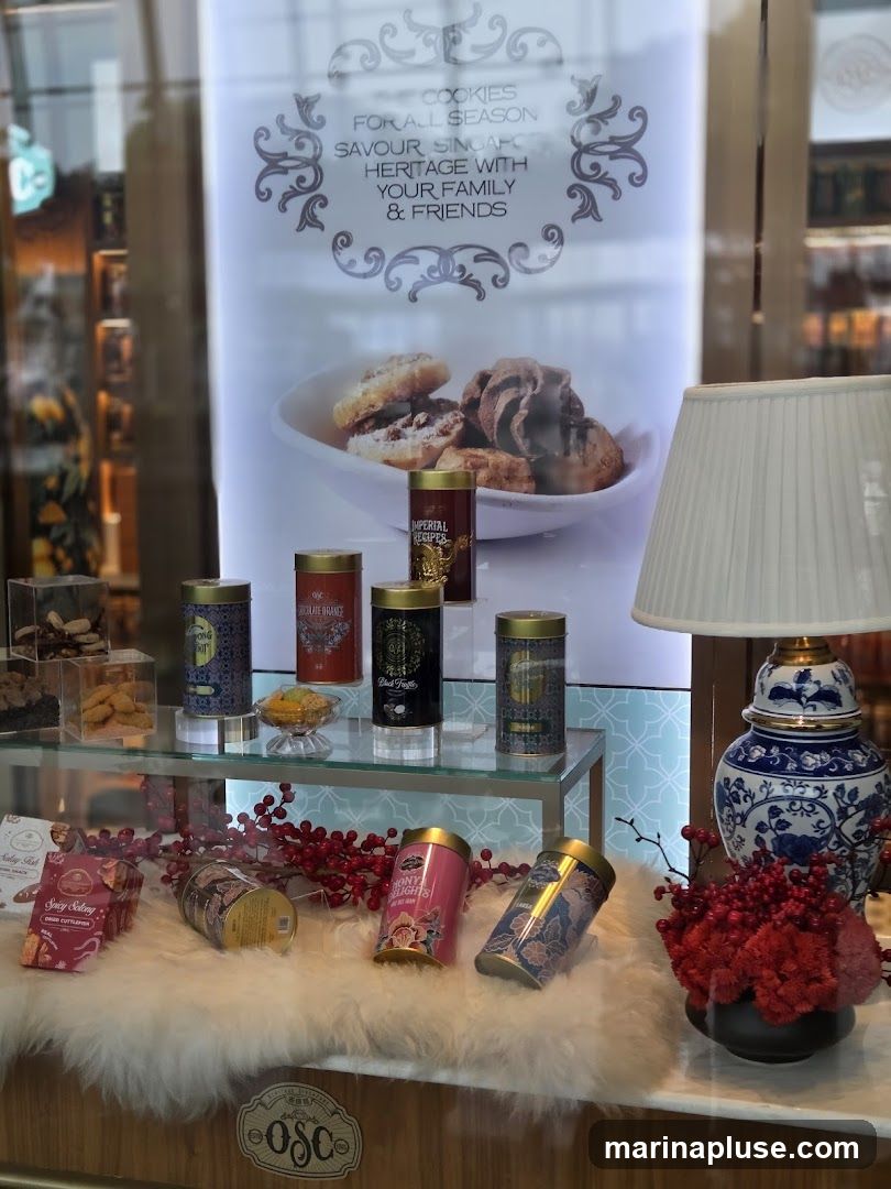 A display window featuring various tins and boxes of cookies, along with decorative elements like red berries and a lamp. A banner advertises "Cookies for All Season" and "Savour Singapore Heritage".