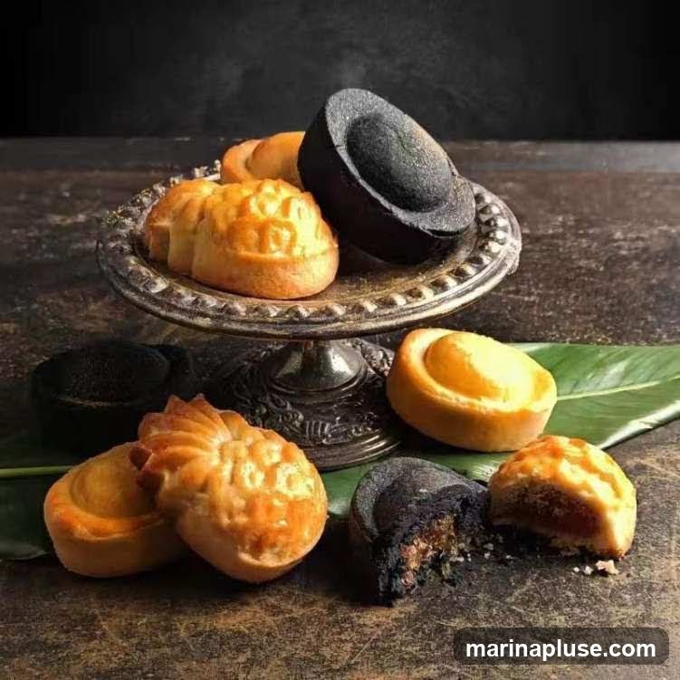 A still life arrangement of various mooncakes, some whole and some cut open, displayed on a rustic surface and a silver cake stand. The mooncakes vary in color and filling, with some appearing to be traditional baked mooncakes and others with a darker, possibly charcoal-infused crust. A large green leaf serves as a backdrop for some of the pastries.