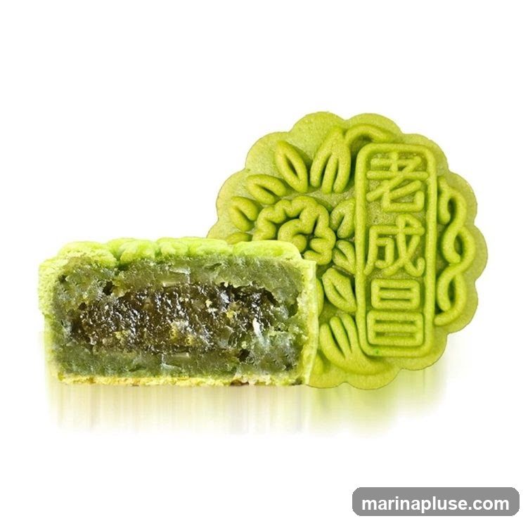 A cross-section of a green mooncake is shown next to a whole mooncake. The mooncake has a floral design and Chinese characters embossed on its surface. The filling appears to be a dark green paste with visible pieces of ingredients.