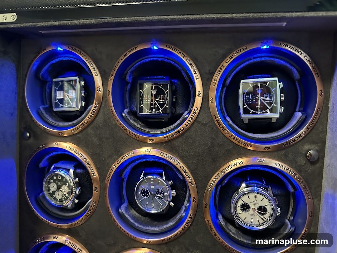 A watch winder with six compartments, each holding a watch. The compartments are illuminated with blue LED lights and have copper-colored trim with the text "ORIENT CROWN" embossed on them.