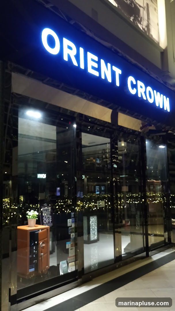 A brightly lit sign above a storefront reads "ORIENT CROWN". The storefront features large glass windows reflecting the interior and exterior lights. Inside, a display case with a wooden exterior holds items, and a potted plant sits on top. A sign on the window indicates "SALES 25% OFF".