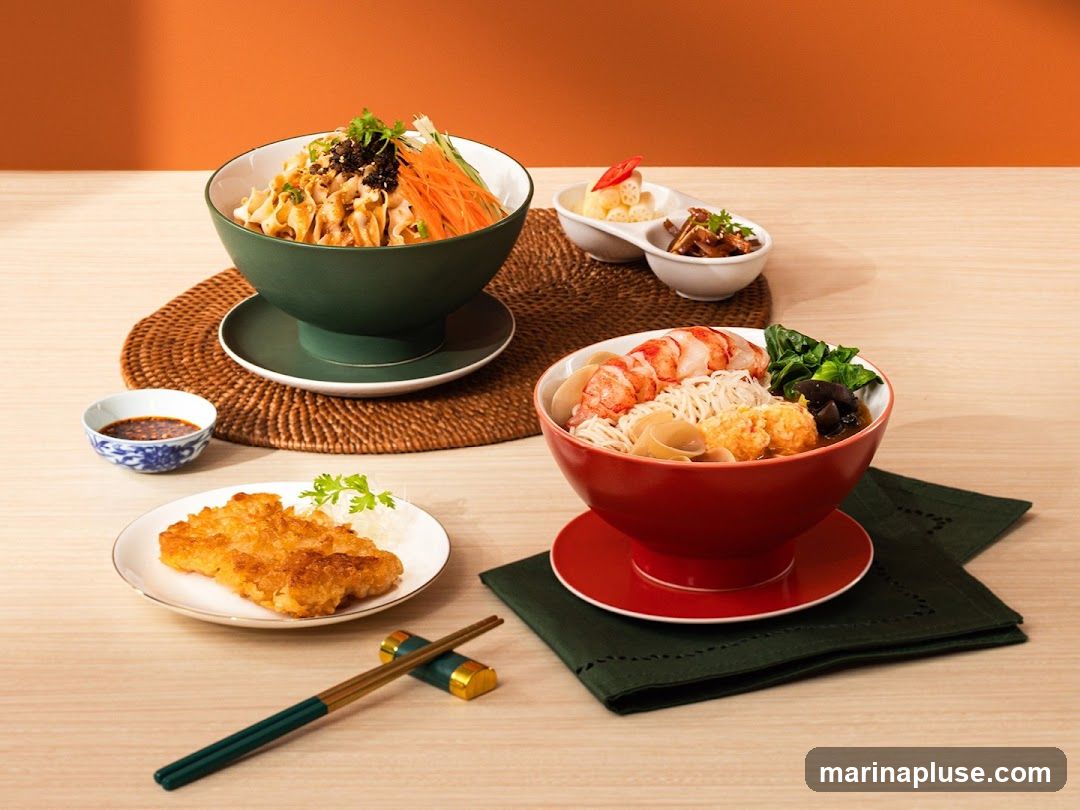 A spread of Asian-inspired dishes, including two bowls of noodles and a fried cutlet. One noodle bowl is dark green and contains noodles with shredded carrots, greens, and a dark topping. The other is red and filled with noodles, large shrimp, fish balls, mushrooms, and greens. A small plate holds a golden-brown fried cutlet with a side of shredded white radish and parsley. A small dish of dipping sauce and chopsticks with a rest complete the arrangement. The background is a warm orange wall and a light wood table.