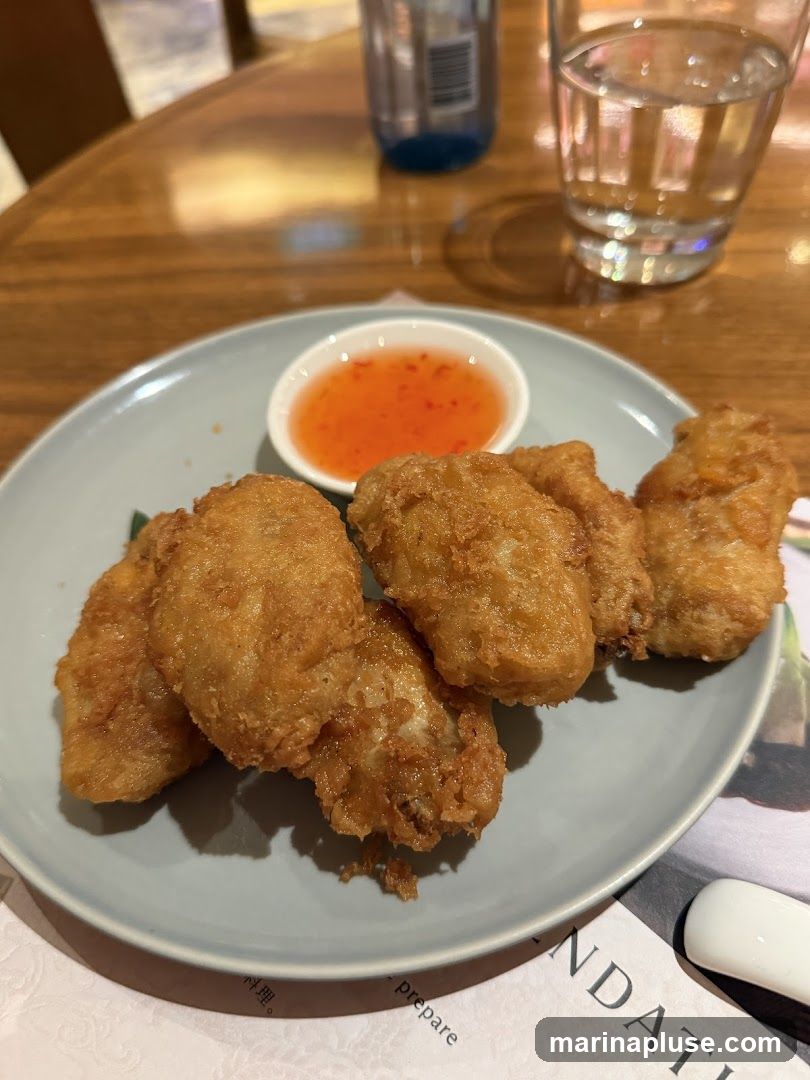 A plate of golden-brown fried food, possibly chicken nuggets or fish bites, is served with a small dish of sweet chili sauce. A glass of water and a bottle of beverage are visible in the background on a wooden table. A printed menu or document is partially visible beneath the plate.