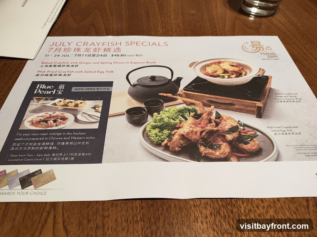 A menu featuring July Crayfish Specials from Tong Dim Noodle Bar. It highlights two crayfish dishes: Baked Crayfish with Ginger and Spring Onion in Superior Broth, and Wok Fried Crayfish with Salted Egg Yolk. The menu also includes information about Blue Pearl seafood restaurant, its opening hours, and location.
