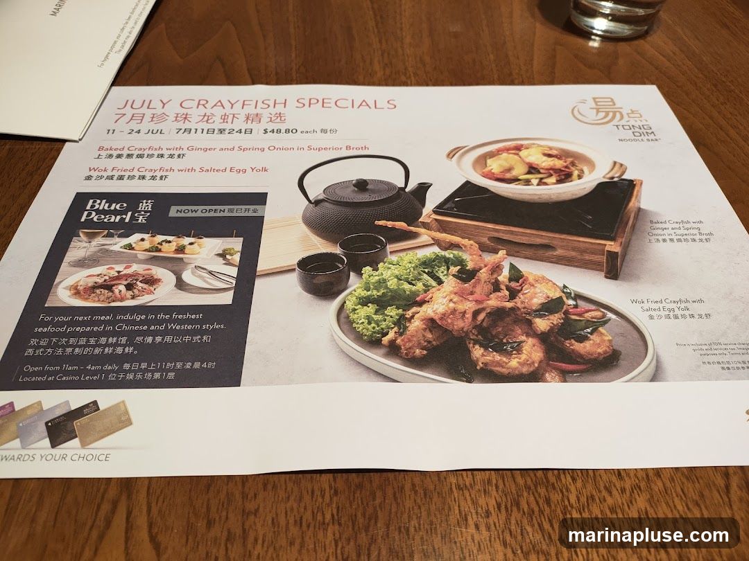 A menu featuring July Crayfish Specials from Tong Dim Noodle Bar. It highlights two crayfish dishes: Baked Crayfish with Ginger and Spring Onion in Superior Broth, and Wok Fried Crayfish with Salted Egg Yolk. The menu also includes information about Blue Pearl seafood restaurant, its opening hours, and location.