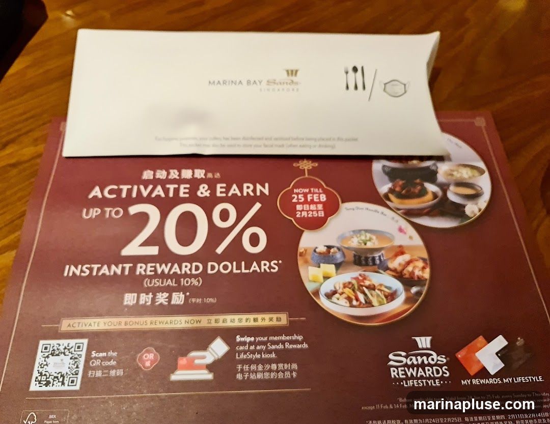 A promotional flyer for Marina Bay Sands Rewards, advertising an offer to activate and earn up to 20% instant reward dollars. The promotion is valid until February 25th. It includes instructions on how to activate rewards via QR code or Sands Rewards LifeStyle kiosk. Images of food dishes are displayed.