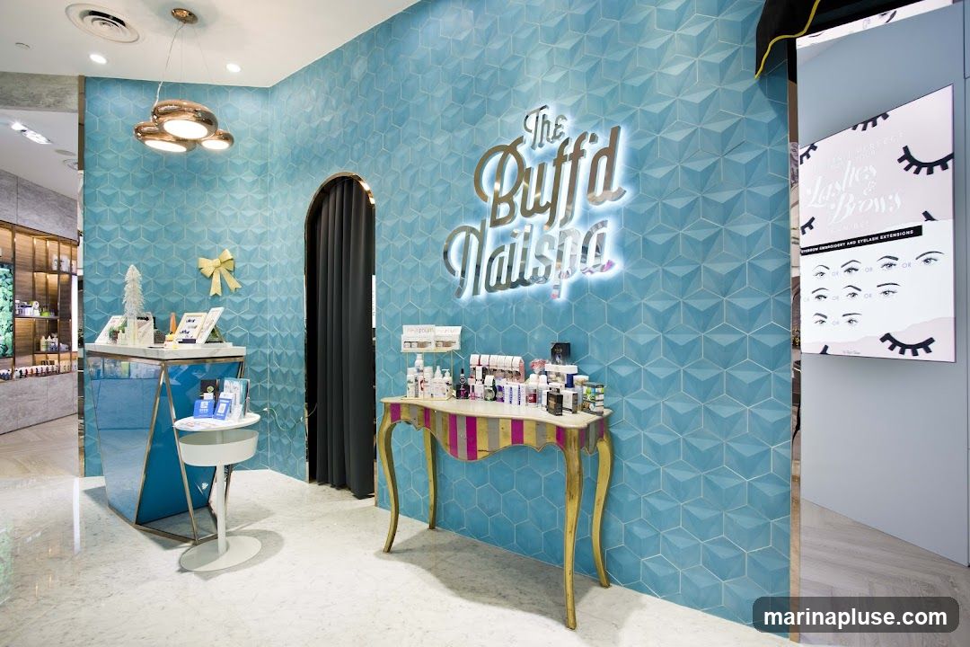 The interior of a nail spa with a prominent turquoise geometric tiled wall. A silver illuminated sign reads "The Buff'd Nailspa".  Various beauty products are displayed on a striped console table and a tiered display stand. To the right, a digital screen shows information about lash and brow services with illustrations of different eyebrow shapes.