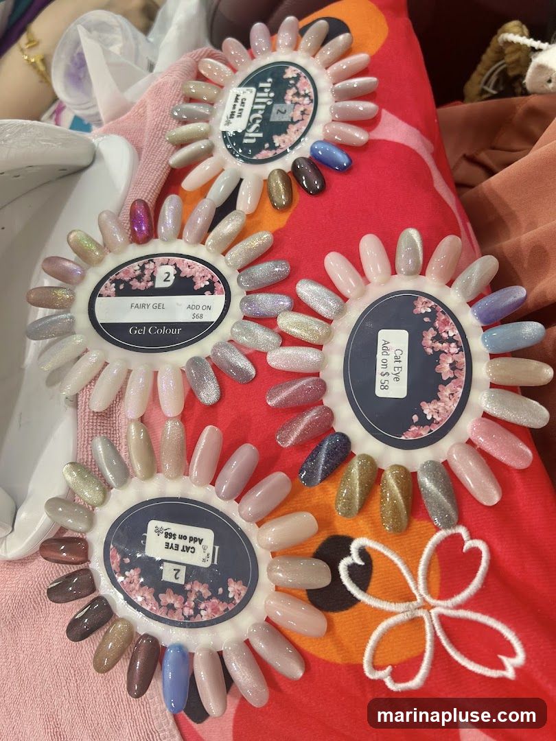 A collection of nail polish swatches displayed on circular wheels. The swatches represent various colors and finishes, including shimmery, glittery, and opaque shades. Some wheels are labeled with terms like "Fairy Gel," "Gel Colour," and "Cat Eye," along with prices for add-ons. The display is set against a red fabric with a floral pattern.