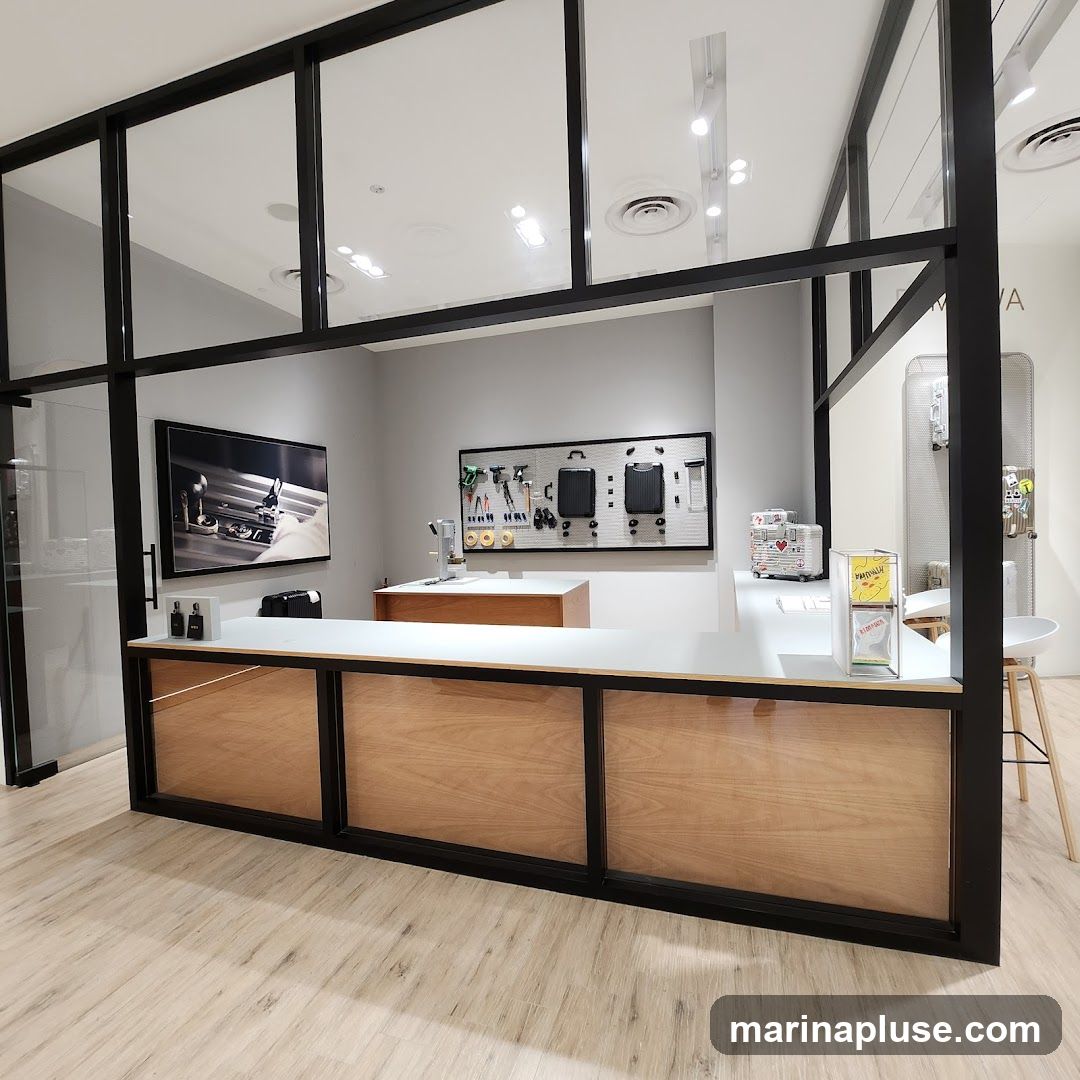 The image shows the interior of a store with a modern design. A long counter with wooden panels is the central feature. Behind the counter, a pegboard displays various tools and two suitcases. A large framed picture hangs on the wall to the left of the pegboard. On the counter, there are some small boxes, a display stand with flyers, and a coffee machine. To the right, a stool and a tall display rack are visible. The overall impression is of a clean and organized retail space, possibly for luggage or travel accessories.