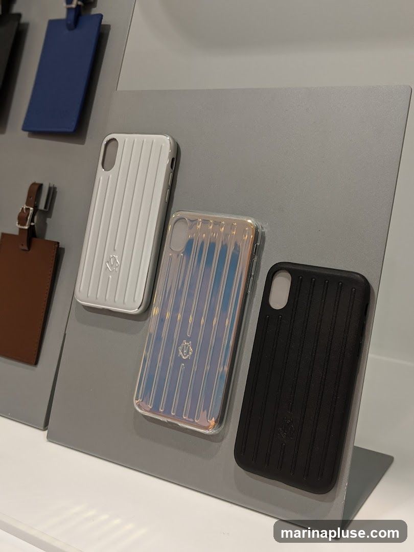 A display featuring several iPhone cases and luggage tags. The phone cases are ribbed and come in white, iridescent, and black. Each case has a small logo in the center. Luggage tags in blue and brown are also visible.