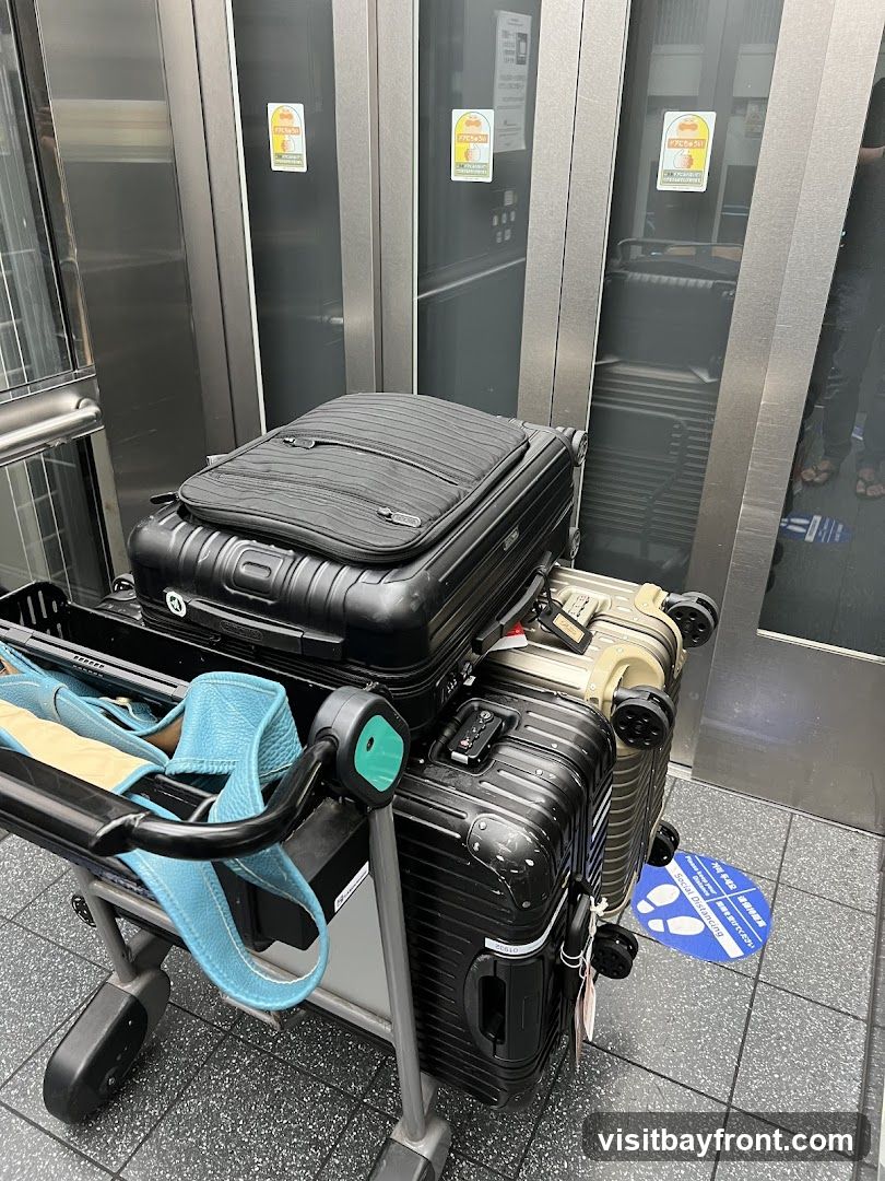 A luggage cart is filled with several suitcases in what appears to be an elevator. The elevator doors are made of reflective metal, and there are yellow stickers with cartoon characters on them. A blue and white floor sticker indicating social distancing is visible on the ground.
