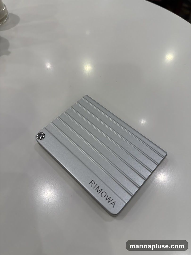 A silver Rimowa card holder with the brand name embossed on it, placed on a white table.