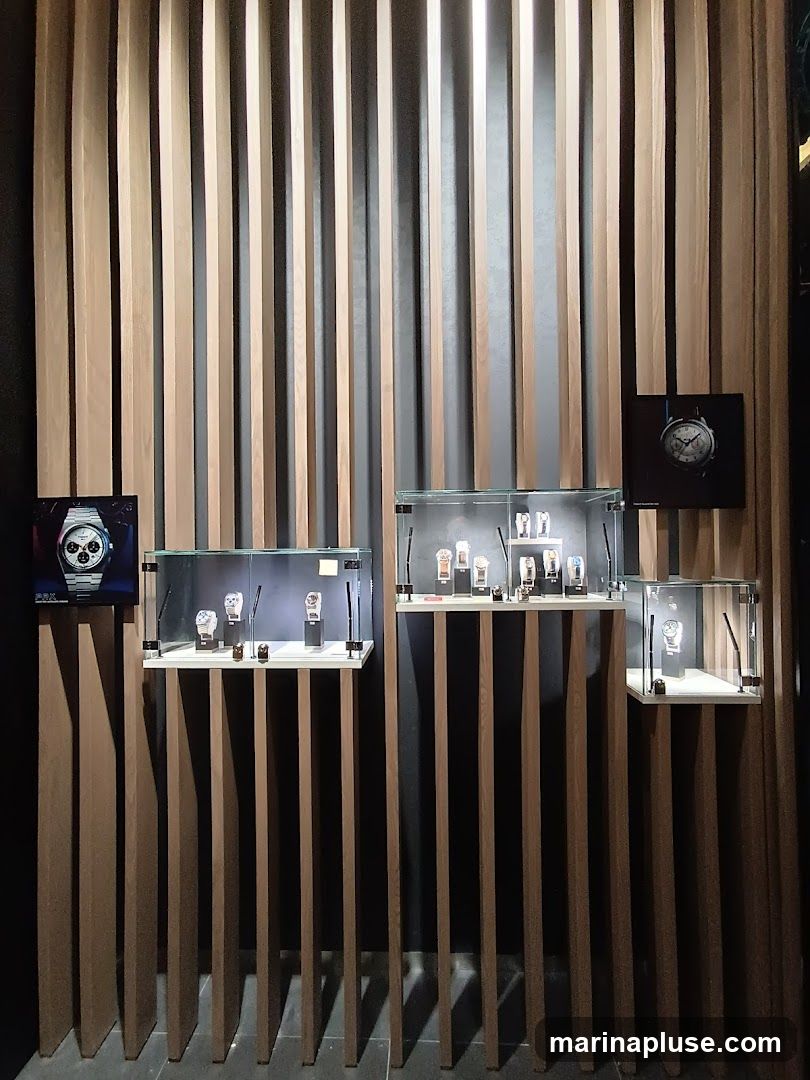 A wall display featuring several glass cases showcasing various watches. The wall is covered with vertical wooden slats. There are also framed images of watches on the wall.