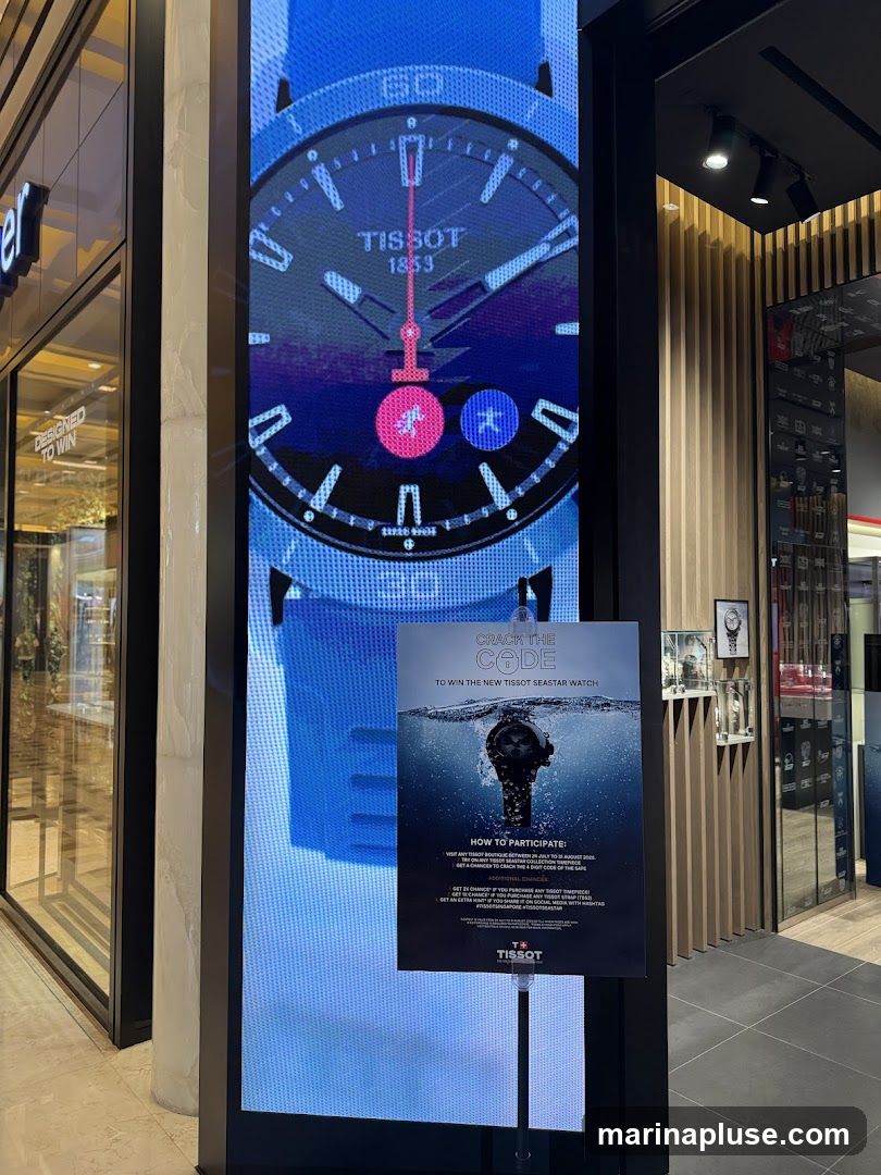 A digital screen displays a close-up of a Tissot watch face with the brand name and year 1853 visible. Below the screen, a poster advertises a contest to win a new Tissot Seastar watch, with instructions on how to participate. The poster features an image of the watch submerged in water. The background shows a store interior with wooden paneling and displays of watches.