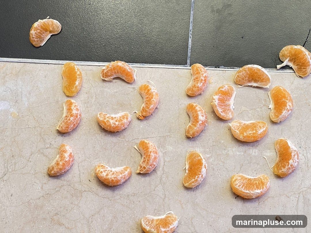 Several peeled mandarin orange segments are scattered on a light-colored, speckled surface, with a dark gray tiled surface above.