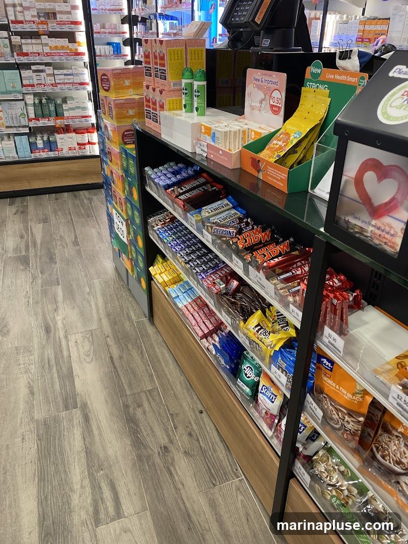 A retail display featuring shelves stocked with various chocolates, candies, and health products. Prominent brands like Hershey's and Mars bars are visible, alongside smaller items such as Eclipse mints and Scott's Vitamin C. In the background, shelves display skincare or pharmaceutical products. A small sign advertises "New & Improved" items for $0.50 each.