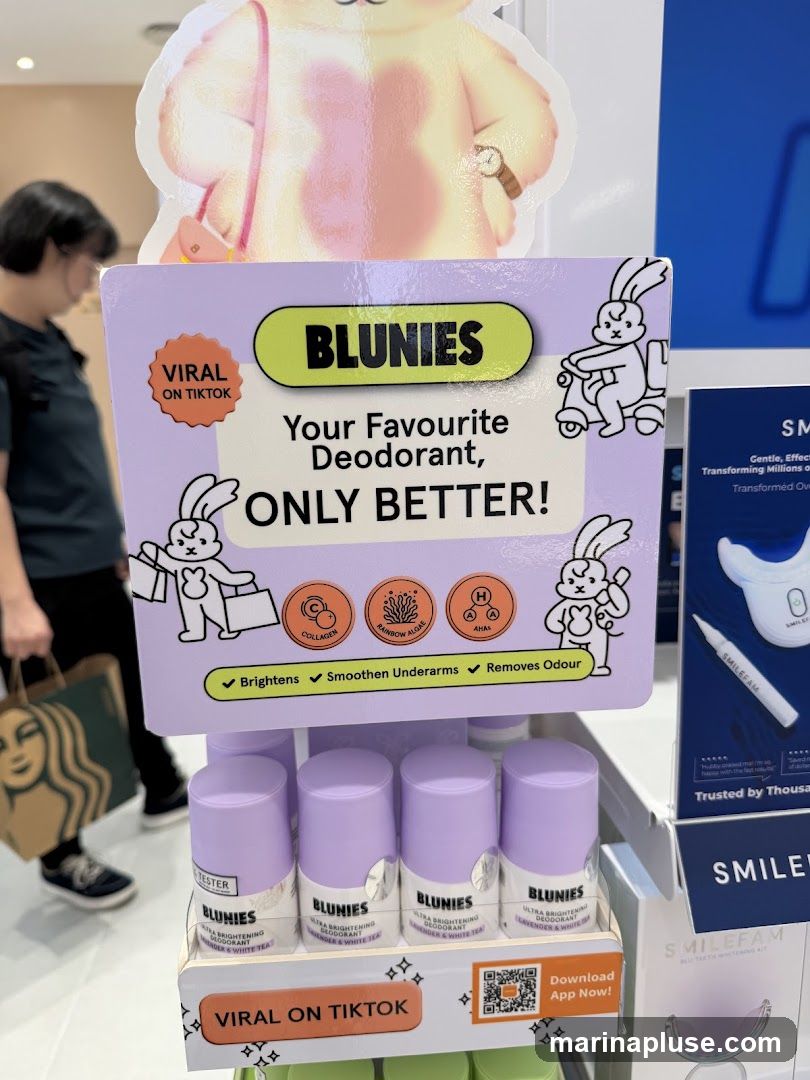 A display stand featuring Blunies Ultra Brightening Deodorant in Lavender & White Tea scent. The display includes cartoon rabbits, icons for Collagen, Rainbow Algae, and AHAs, and text highlighting benefits like brightening and odour removal. A QR code for app download is also visible. In the background, a person walks by carrying a Starbucks bag.