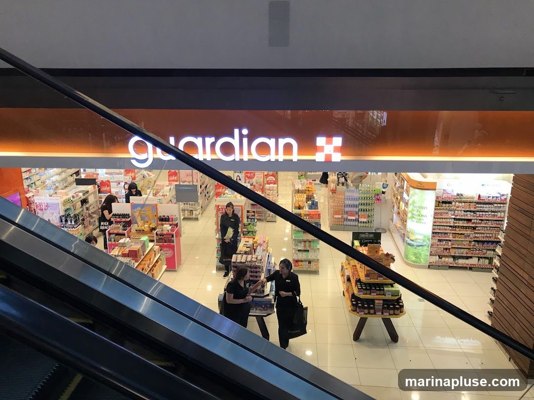 An overhead view of the interior of a Guardian pharmacy, with shelves stocked with various health and beauty products. Several staff members are visible assisting customers and organizing merchandise. The store features bright lighting and a clean, organized layout.