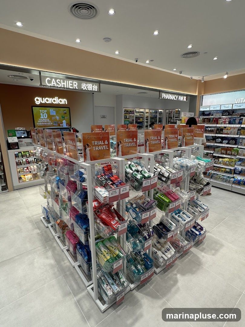 The interior of a Guardian pharmacy with a central display of trial and travel-sized products. Signs indicate "CASHIER" and "PHARMACY". Shelves stocked with various health and beauty products are visible in the background.