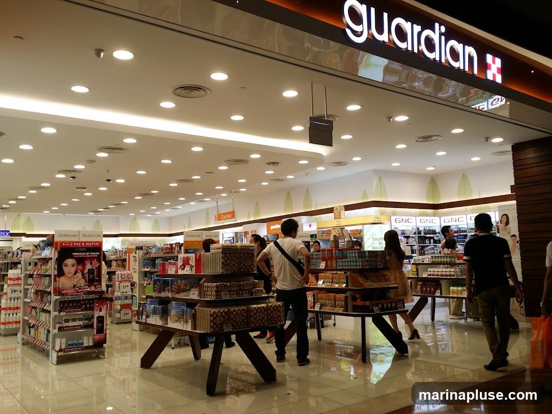 The interior of a Guardian pharmacy with shelves stocked with health and beauty products. Customers are browsing the aisles. The Guardian logo is visible above the entrance.