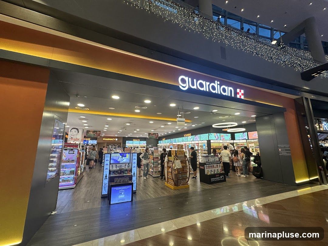 The exterior of a Guardian pharmacy store. The store has a large illuminated sign with the Guardian logo above the entrance. Inside, shelves are stocked with various health and beauty products. Customers are browsing the aisles.
