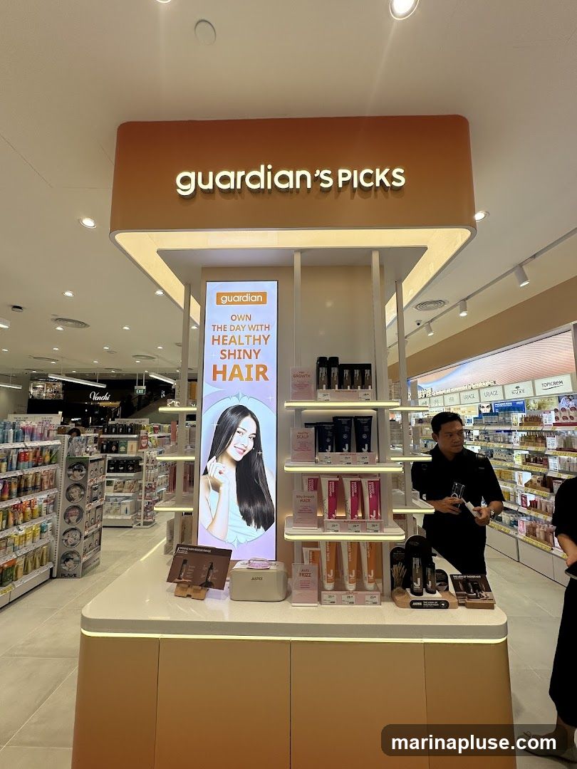 A display stand featuring hair care products under the "Guardian's Picks" branding. A large illuminated panel shows a woman with healthy, shiny hair and the text "OWN THE DAY WITH HEALTHY SHINY HAIR". Various hair care products are arranged on shelves. A staff member is visible on the right side of the image.