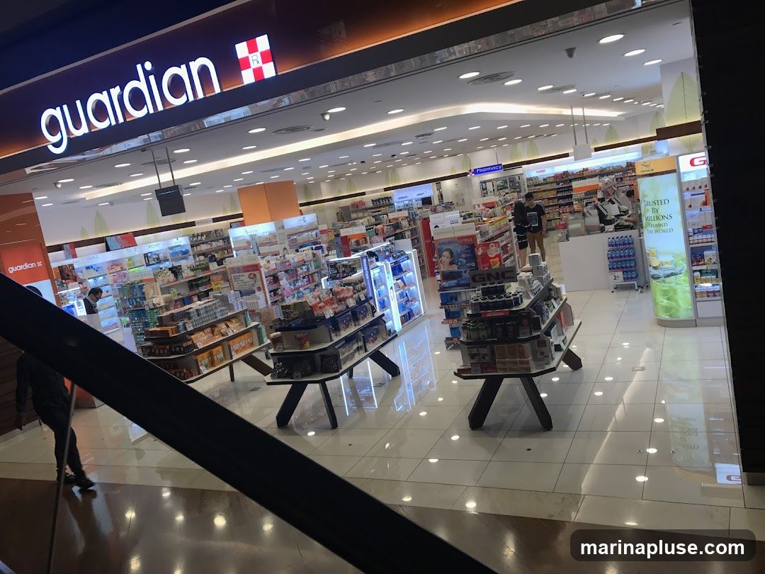 The exterior of a Guardian pharmacy is visible, with its prominent illuminated signage displaying the brand name. Inside, the store is well-lit and stocked with a wide variety of health and beauty products displayed on shelves and gondolas. Several customers and staff members are seen browsing and working within the store.