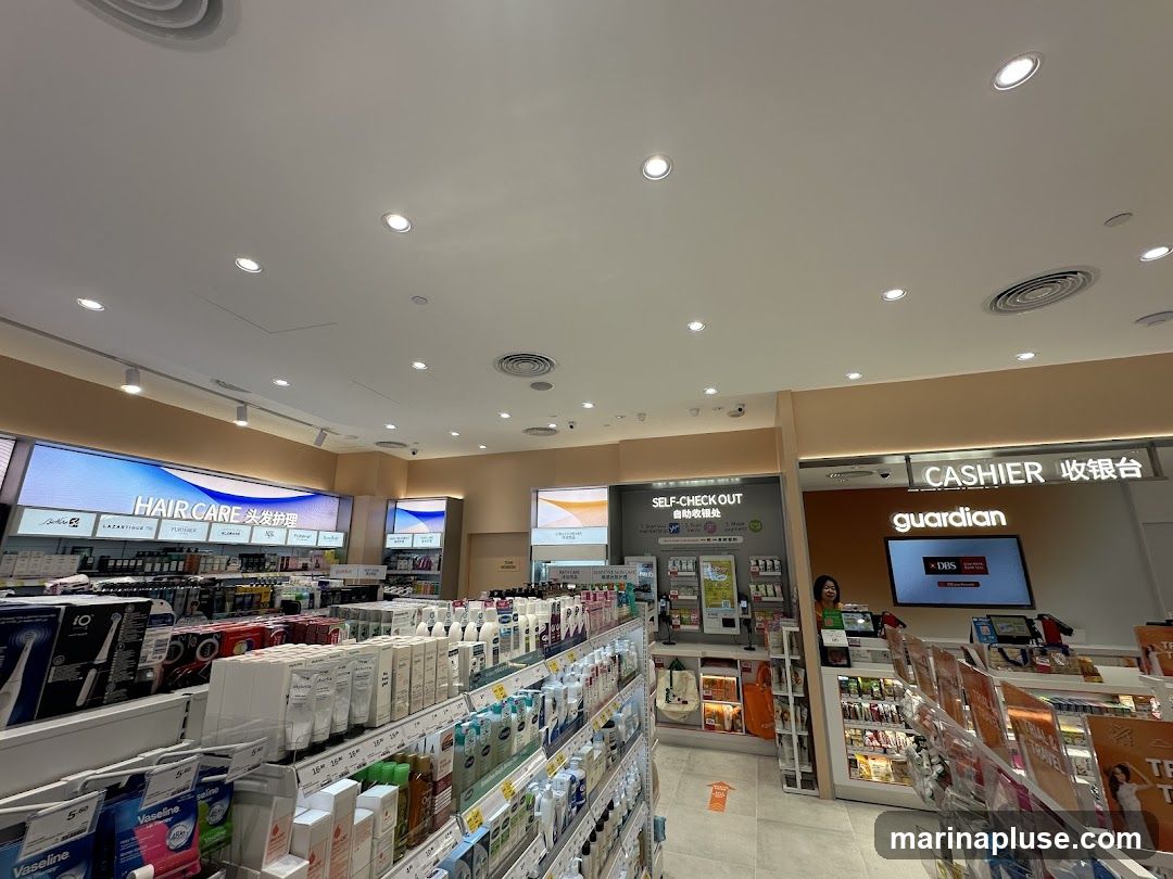 The interior of a Guardian pharmacy, showcasing aisles stocked with health and beauty products. A 'Hair Care' display is visible on the left, and a 'Self-Check Out' area and 'Cashier' counter with the Guardian logo are on the right. A staff member is visible at the cashier counter.