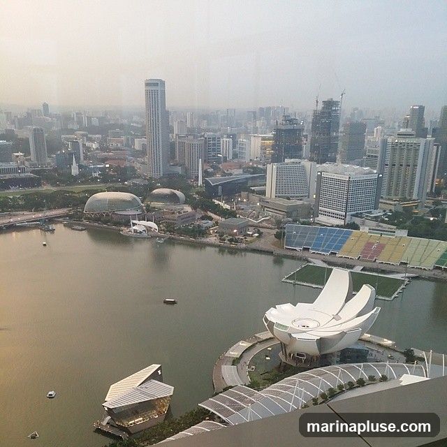 An aerial view of a city skyline with a body of water in the foreground. Several modern buildings, including skyscrapers and a distinctive lotus-shaped structure, are visible. The water reflects the hazy sky and surrounding structures. Boats are scattered across the water. In the background, a dense urban landscape stretches to the horizon.