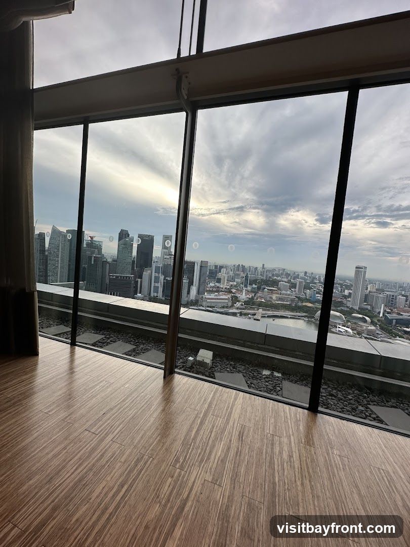 A panoramic view of a city skyline is seen through large, angled windows. The foreground features a polished wooden floor. The cityscape includes numerous tall buildings and a body of water, with a cloudy sky overhead.