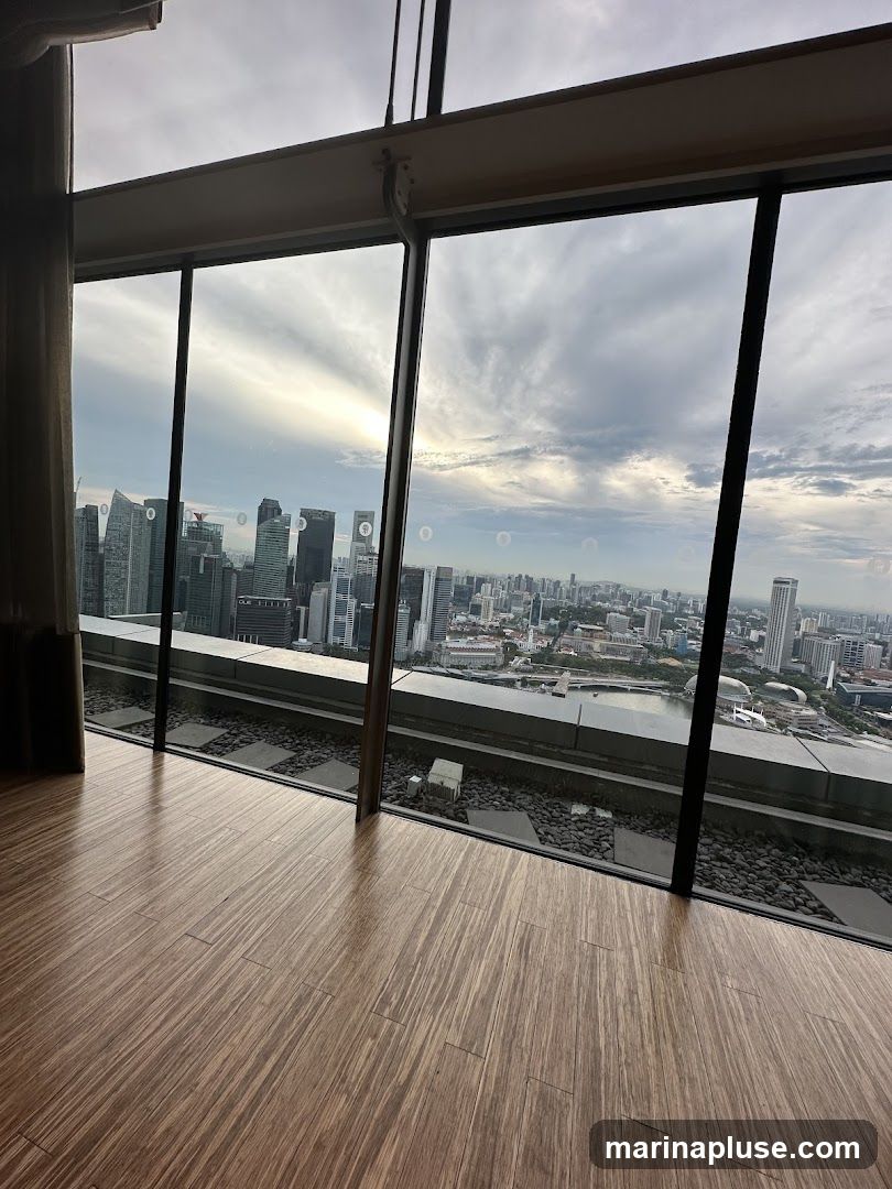 A panoramic view of a city skyline is seen through large, angled windows. The foreground features a polished wooden floor. The cityscape includes numerous tall buildings and a body of water, with a cloudy sky overhead.