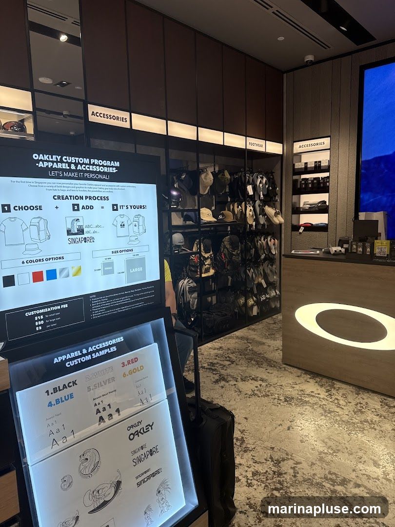 A display showcasing the Oakley Custom Program for apparel and accessories. It details the creation process of choosing an item, adding personalization, and the final product. Options for colors, sizes, and customization fees are listed. Samples of custom text and graphics are also displayed, along with various Oakley accessories and footwear in the background.