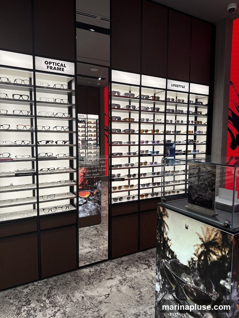 A well-lit interior of an eyewear store showcasing a wide selection of optical frames and lifestyle sunglasses. The frames are neatly arranged on shelves under illuminated signs that read "OPTICAL FRAME" and "LIFESTYLE". A mirrored section reflects more displays, and a large graphic print featuring sunglasses and a rocky landscape is visible.