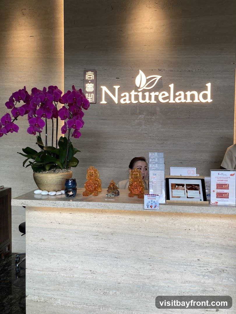 A reception desk with the Natureland logo illuminated above it. A woman is partially visible behind the desk. On the desk are decorative items, a tablet displaying images, and promotional flyers.