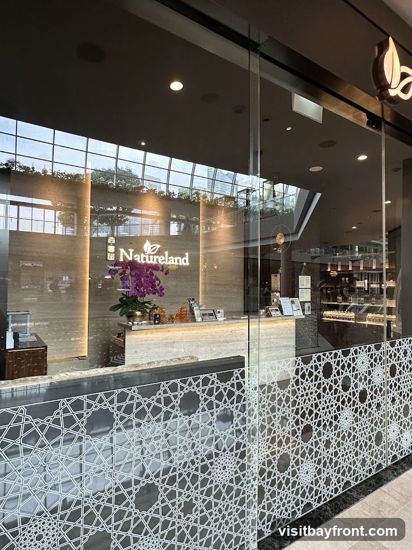 A view through a glass storefront into a well-lit reception area. The shop's name, "Natureland," is prominently displayed on a marble-clad wall behind a reception desk. A large floral arrangement adds a touch of color. The lower part of the glass features an intricate white geometric pattern.