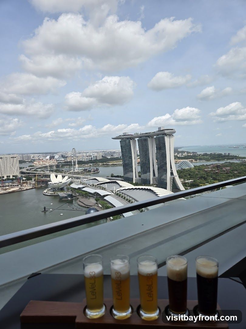 A flight of five beers is presented on a wooden tray in the foreground, with the Singapore skyline and Marina Bay Sands in the background. The glasses are labeled "Level33". The sky is partly cloudy.